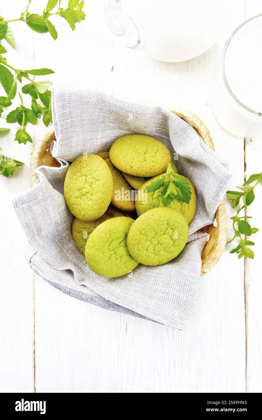 Biscotti alla menta verde su un tovagliolo in un cestino di vimini, latte in un bicchiere e una caraffa sullo sfondo di legno chiaro dall'alto Foto Stock Biscotti alla menta verde su un tovagliolo in un cestino di vimini, latte in un bicchiere e una caraffa sullo sfondo di legno chiaro dall'alto Foto Stock