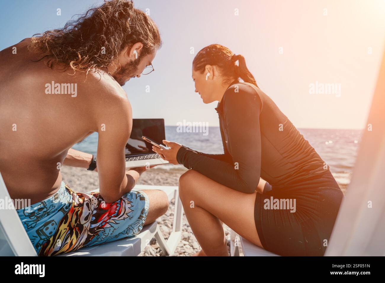 Laptop da lavoro di coppia in spiaggia - i nomadi digitali lavorano in spiaggia con laptop e telefono Foto Stock