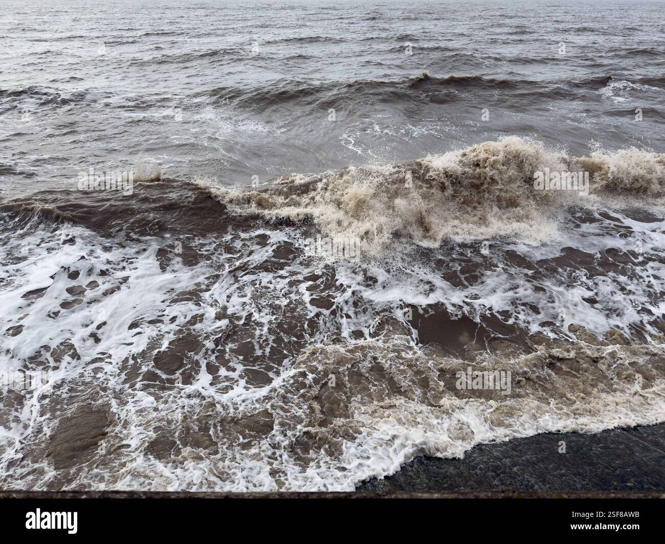 Onde che si infrangono sulla marea in arrivo contro il muro del mare Foto Stock