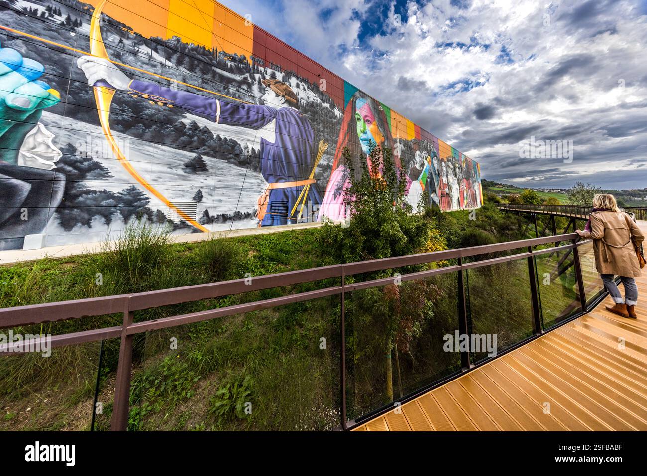 Un passaggio pedonale a San Marino presenta un grande murale sull'esterno di un edificio che raffigura figure storiche e scene Che Una persona cammina lungo il passaggio che guarda il murale. Strada del Sabattino, San Marino Foto Stock