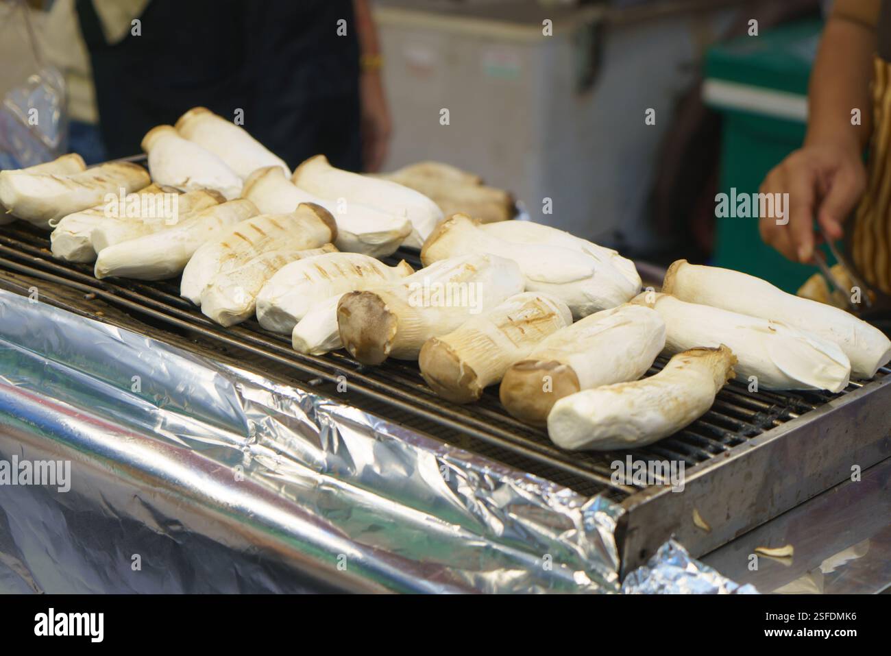 primo piano di grandi funghi di ostriche king grigliati su un barbecue caldo in un vivace chiosco di cibo di strada. La loro consistenza morbida e sostanziosa e saporita Foto Stock