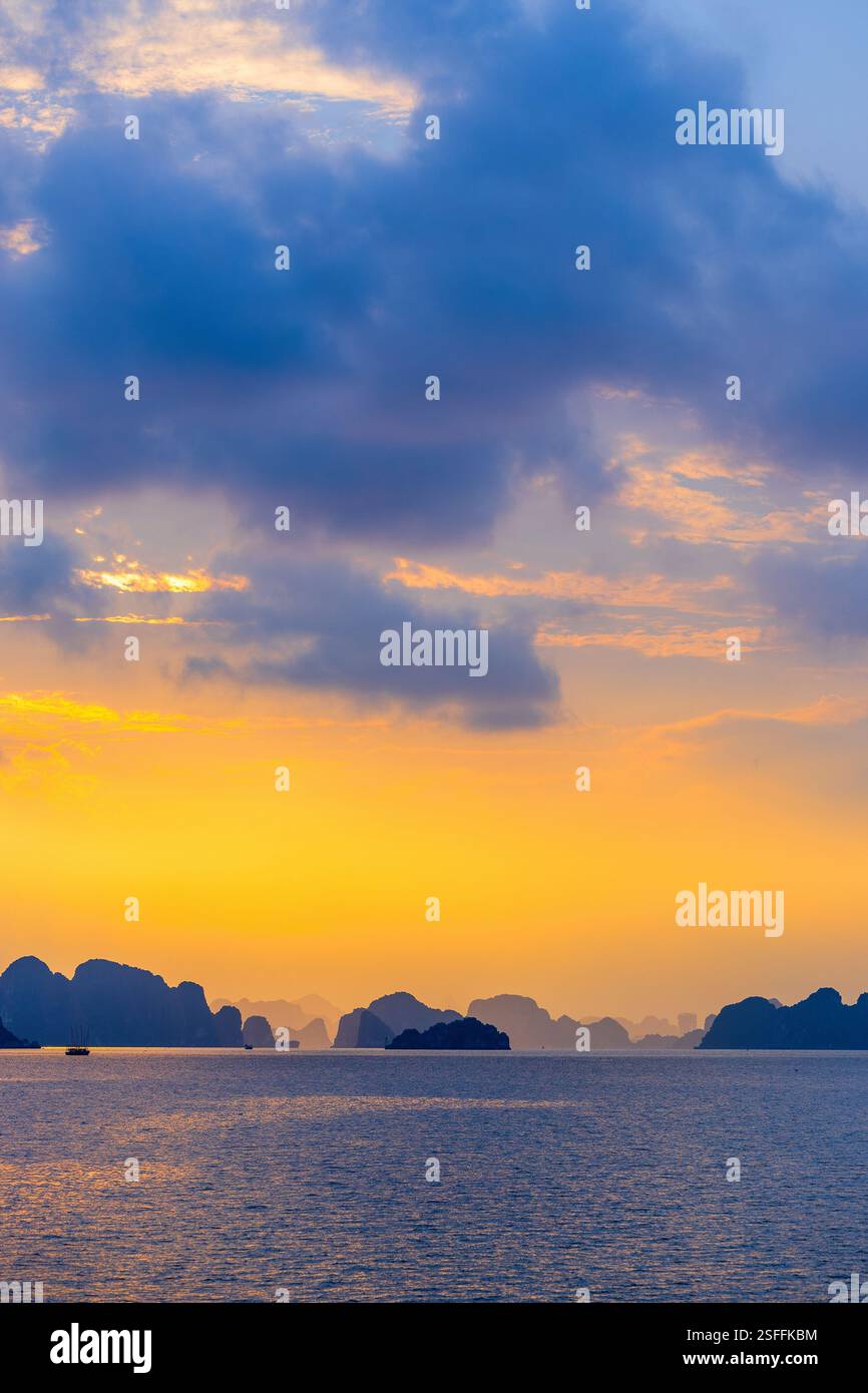 Una splendida vista della Baia di ha Long al tramonto, con il cielo illuminato in calde tonalità dorate. Le isole e le scogliere di pietra calcarea scura si stagliano contro il Foto Stock