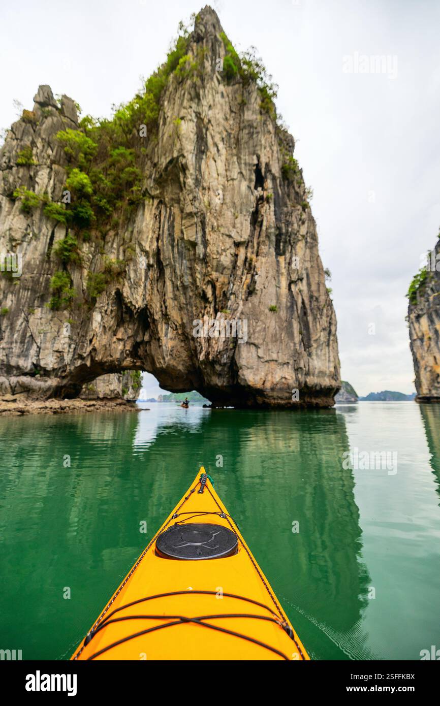 Un kayak si avvicina a un arco calcareo naturale nella baia di ha Long. Scogliere torreggianti e acque verdi e calme creano un ambiente tranquillo ma avventuroso in questo c Foto Stock