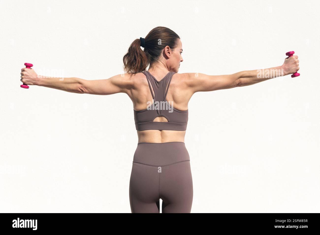 vista posteriore di una donna sportiva che fa l'escissione con piccoli pesi delle mani, tono muscolare. Foto Stock