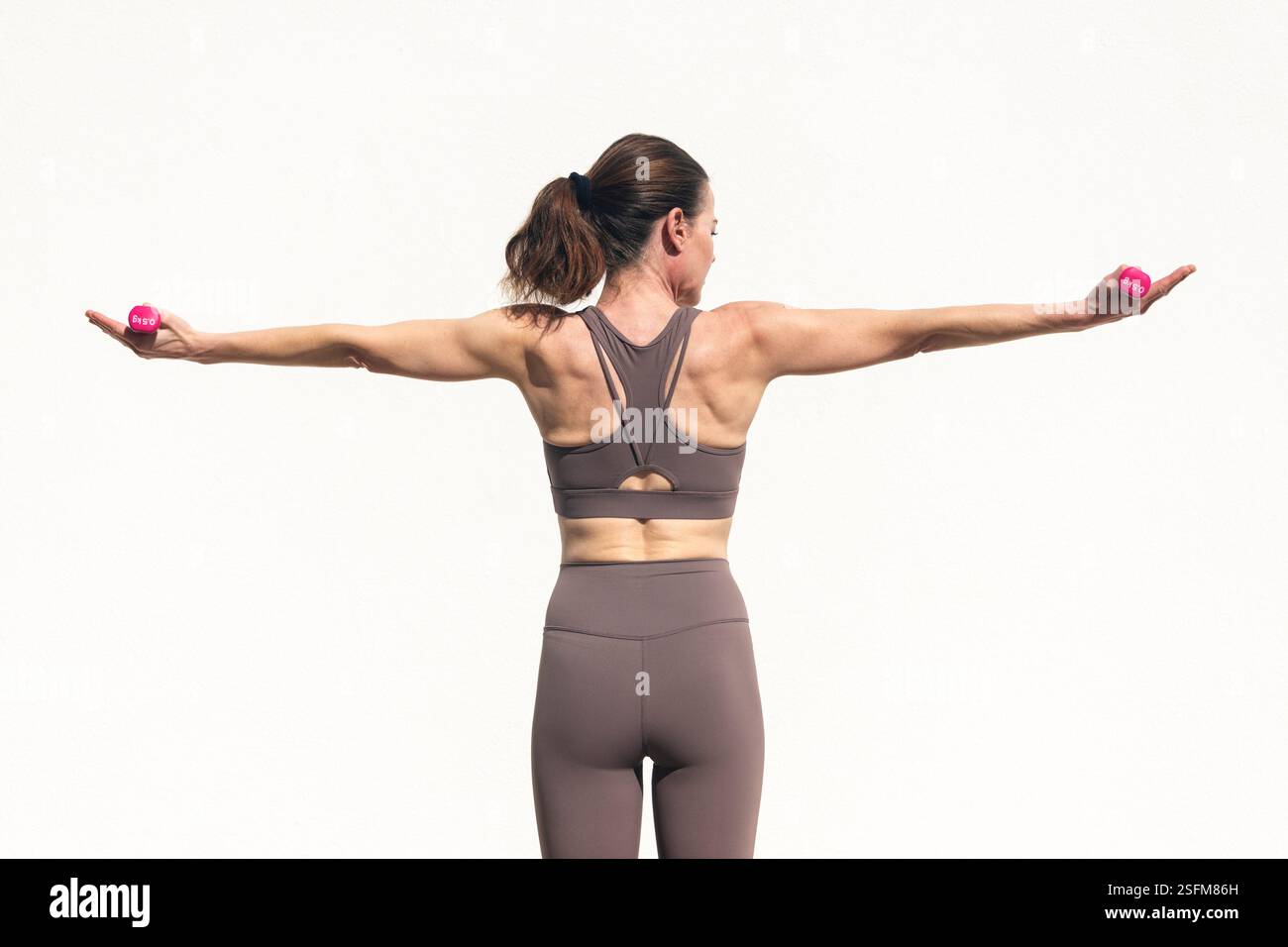vista posteriore di una donna sportiva che fa l'escissione con piccoli pesi delle mani, tono muscolare. Foto Stock