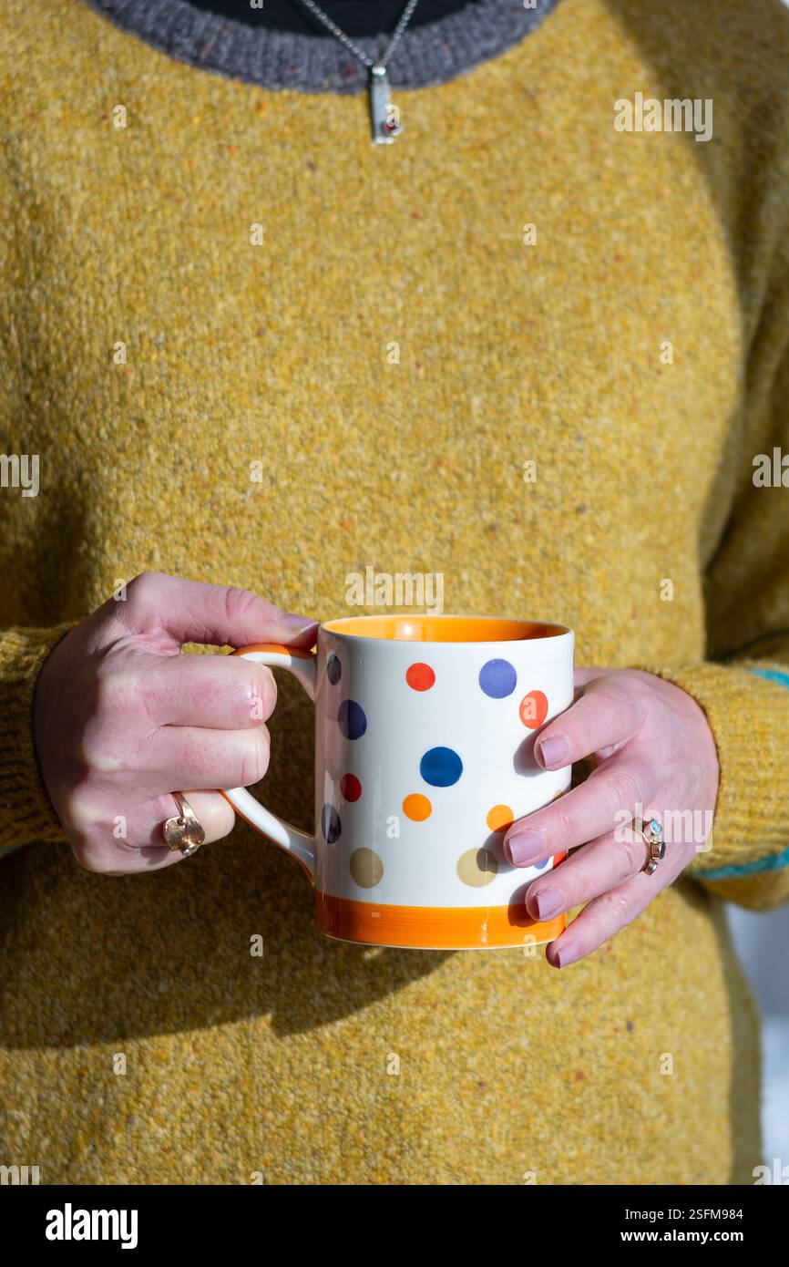 Bristol, Regno Unito. Una donna che tiene in mano una tazza grande di tè o caffè. La tazza calda pesante è supportata da entrambe le mani Foto Stock