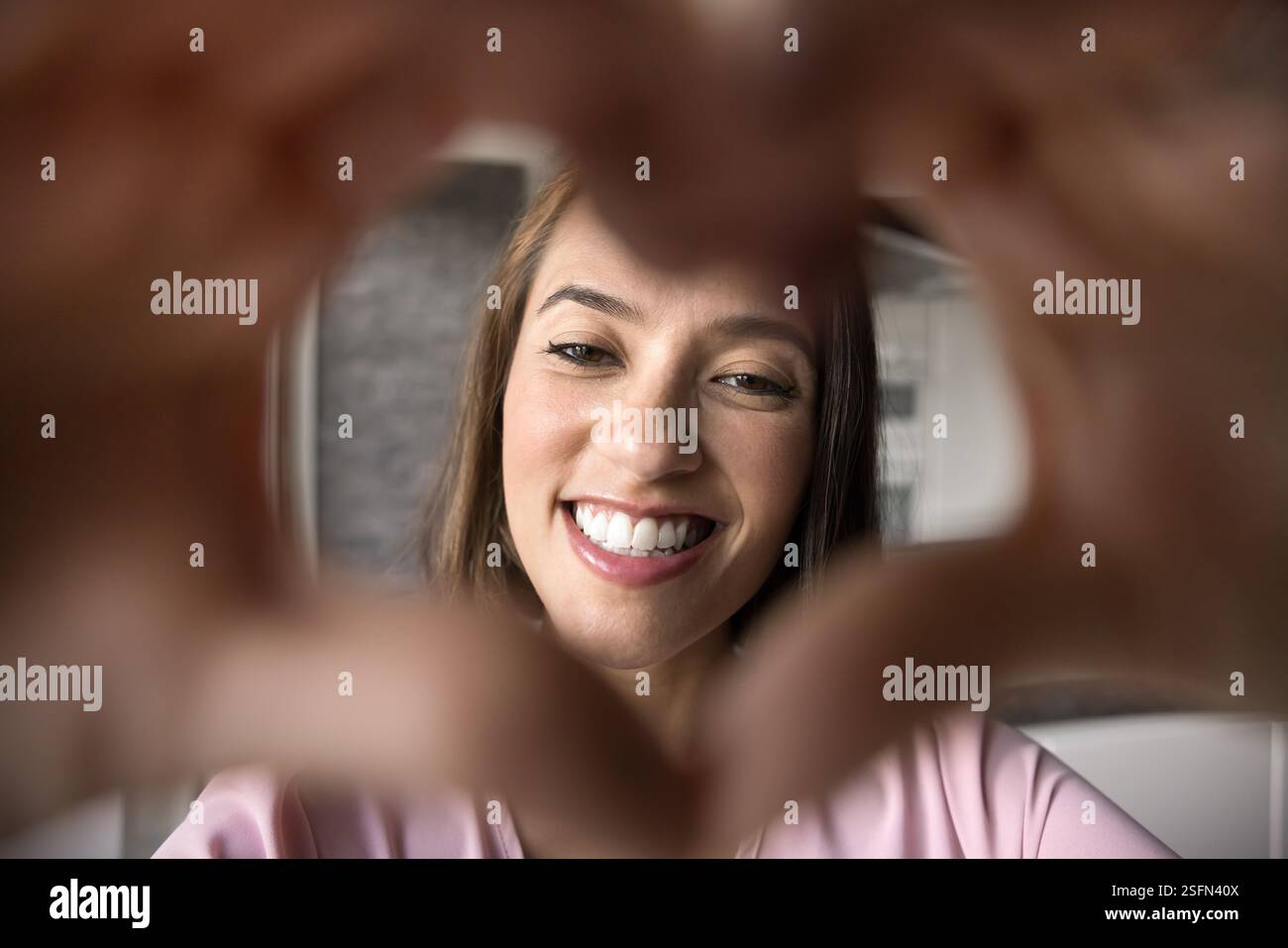 La donna incornicia il suo viso con le mani a forma di cuore Foto Stock