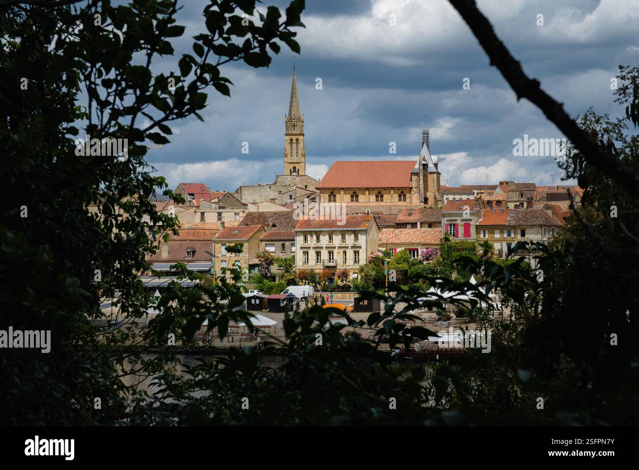 Vista orizzontale della guglia della chiesa di Bergerac, con edifici antichi, finestre, incorniciate da vegetazione Foto Stock