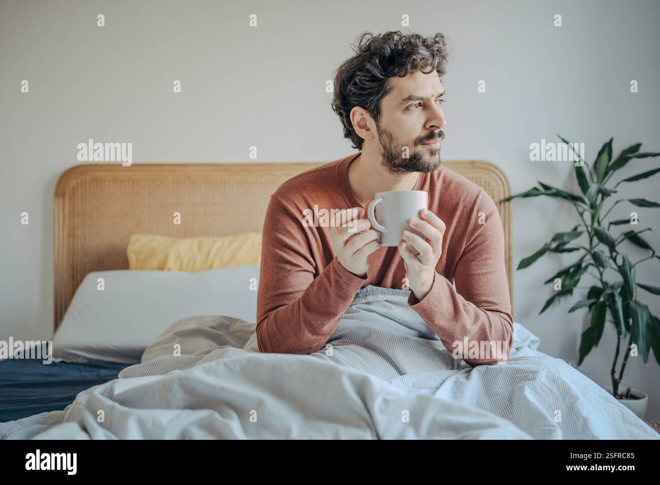 Giovane e rilassato, bell'uomo medio-orientale che si gusta il caffè mattutino a letto. Foto Stock