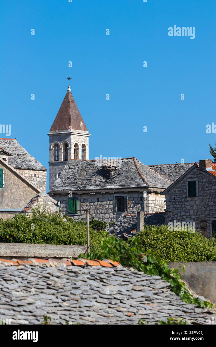 Un pittoresco villaggio caratterizzato da tradizionali edifici in pietra e da un'importante torre della chiesa, adagiata su un cielo azzurro. Foto Stock
