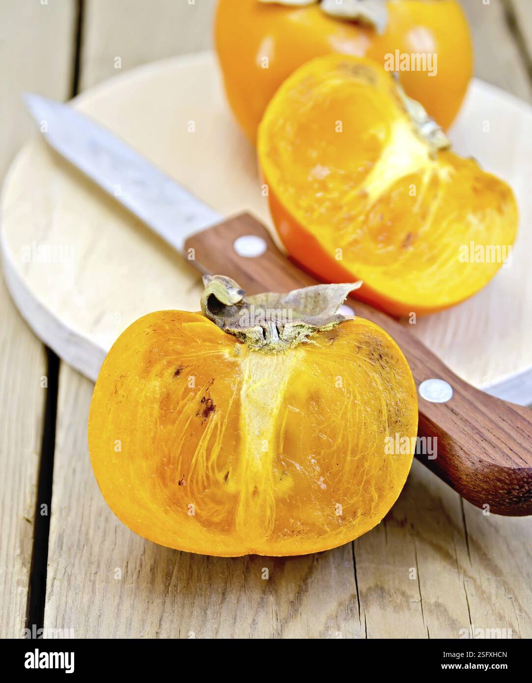 Un frutto intero e mezzo cachi, coltello su una tavola rotonda su uno sfondo di legno Foto Stock