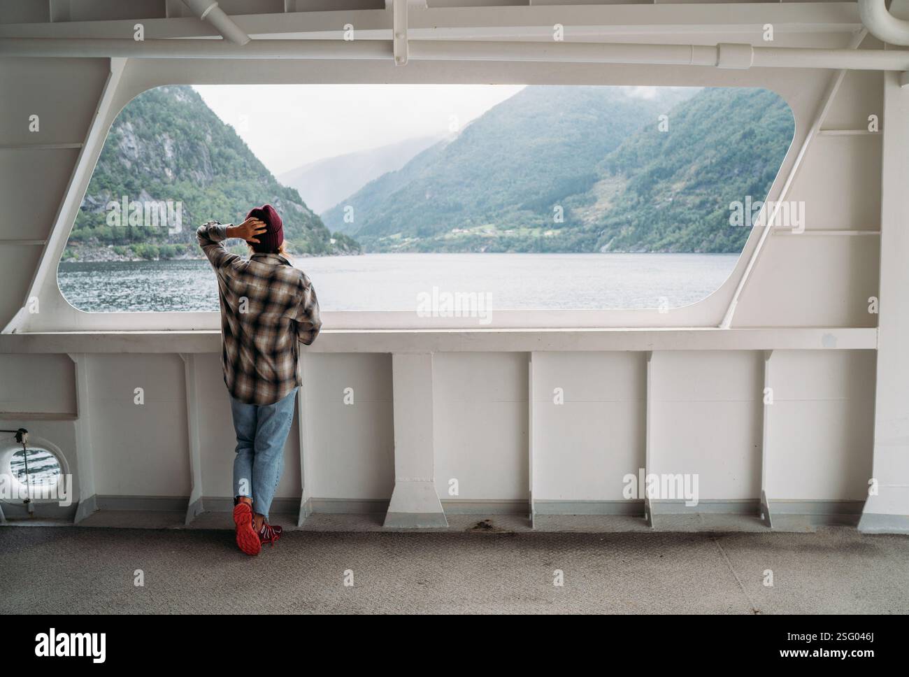 Donna che gode dei paesaggi dei fiordi sul traghetto norvegese con montagne verdi nebbiose sullo sfondo. La scena cattura l'essenza del viaggio rilassato, dell'esplorazione Foto Stock