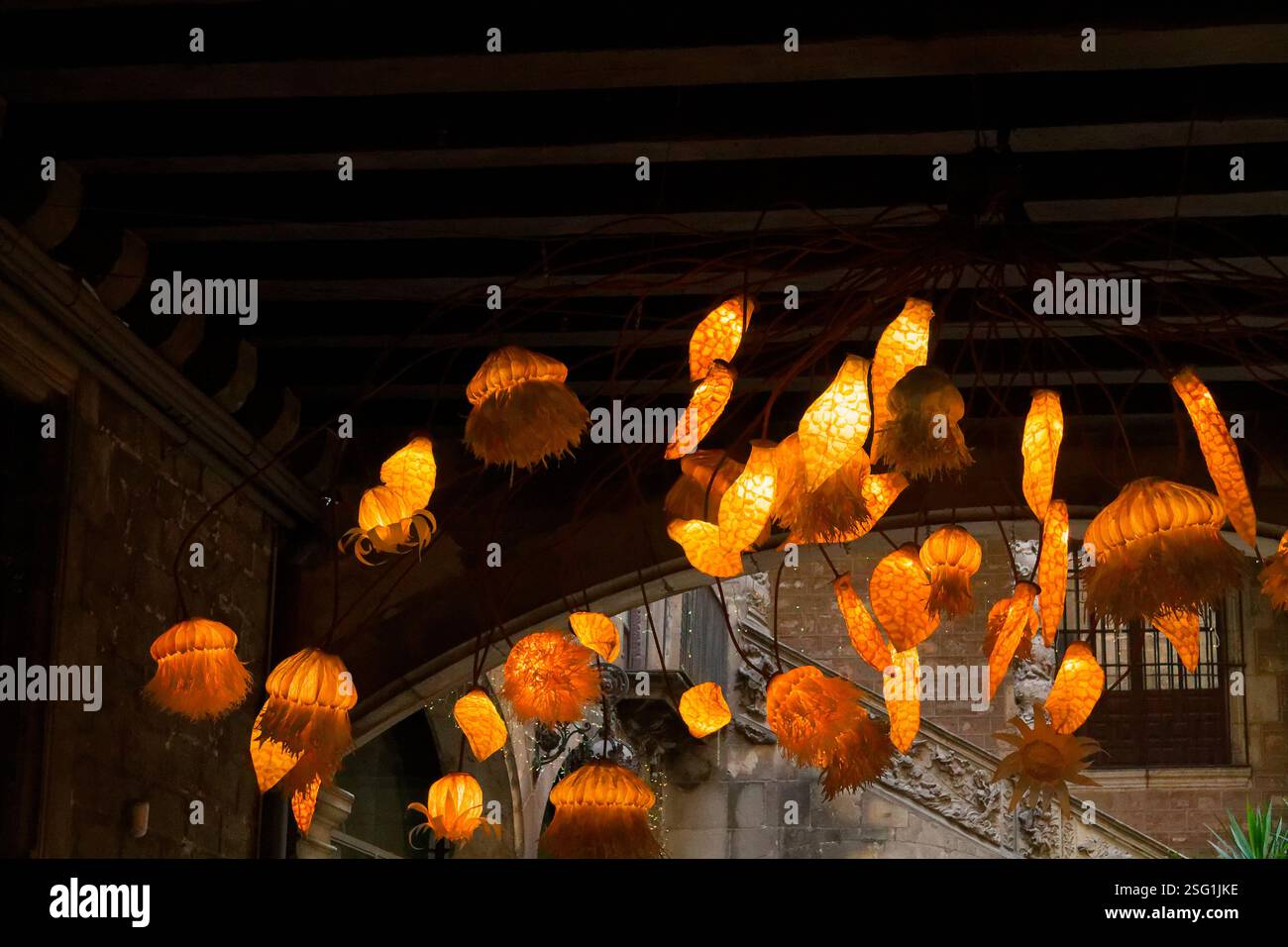 Una splendida esposizione di lampade a sospensione illuminate che ricordano meduse, che proiettano un caldo bagliore dorato in uno spazio poco illuminato con un'architettura rustica. Foto Stock