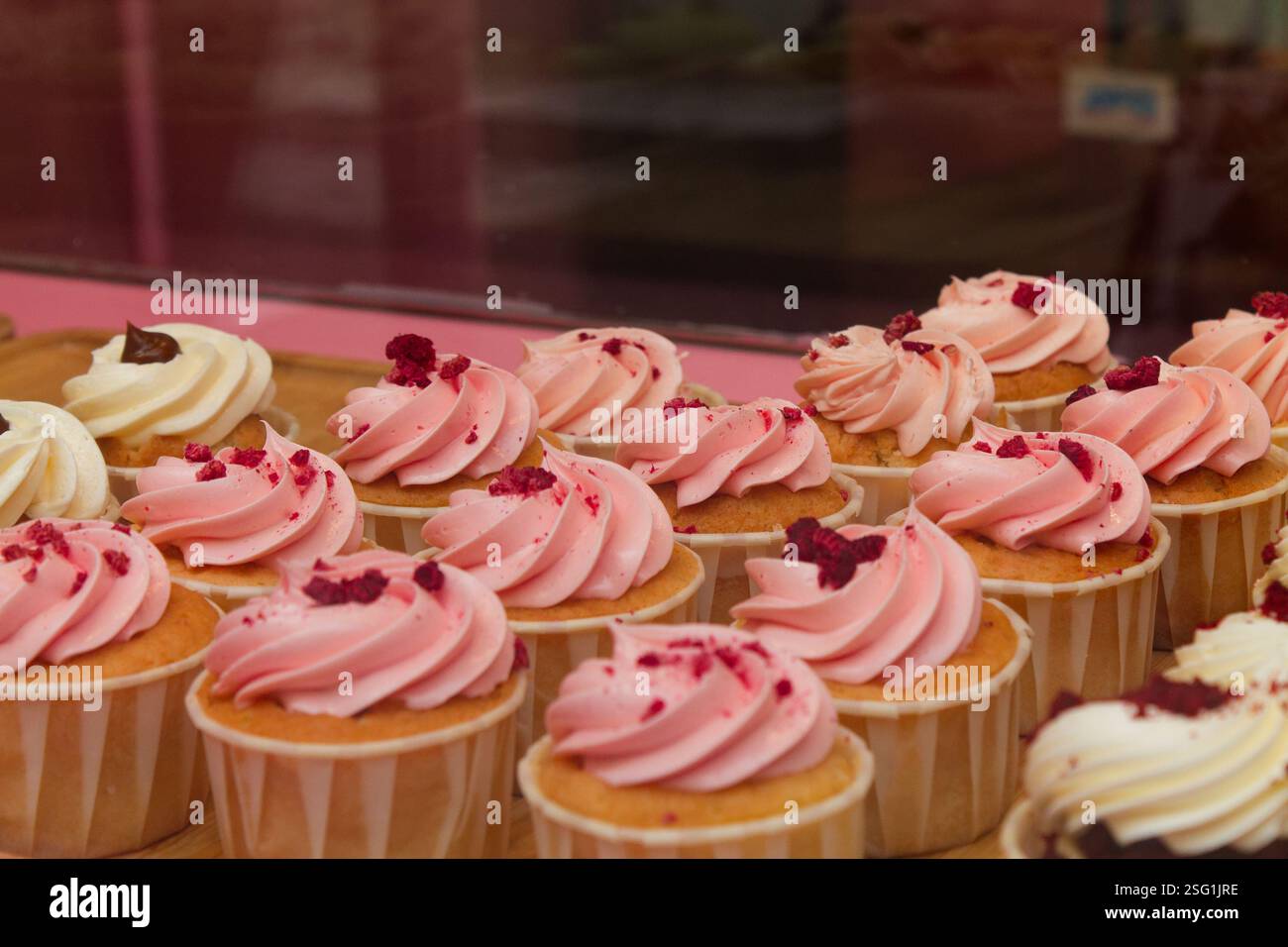 Una selezione di deliziosi cupcake con glassa rosa e bianca, ricoperti di frutti rossi schiacciati. I cupcake sono disposti ordinatamente in fila, mostrando t Foto Stock