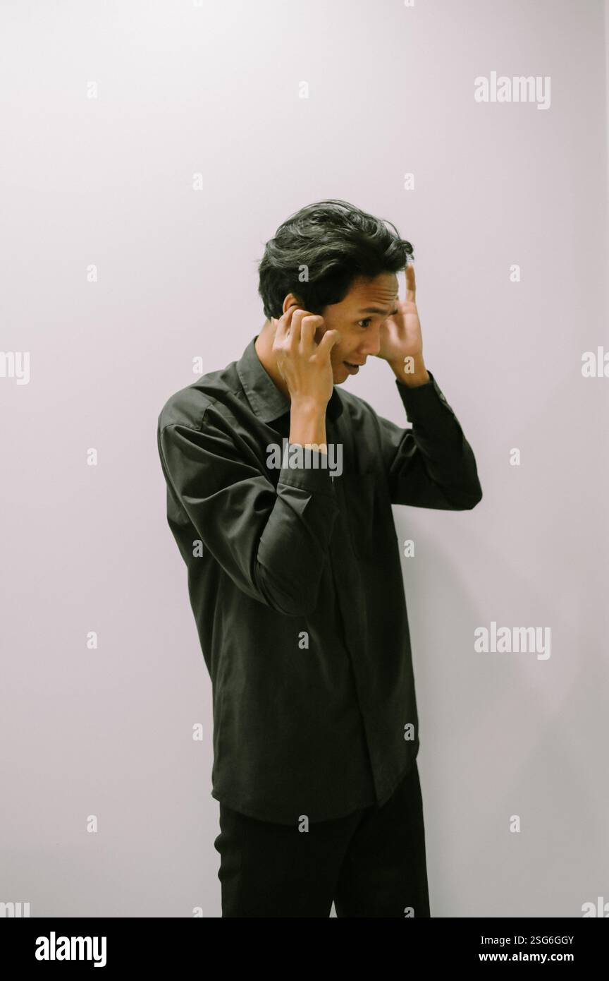 Uomo che copre le orecchie con le mani, camicia nera, sfondo semplice. Foto Stock