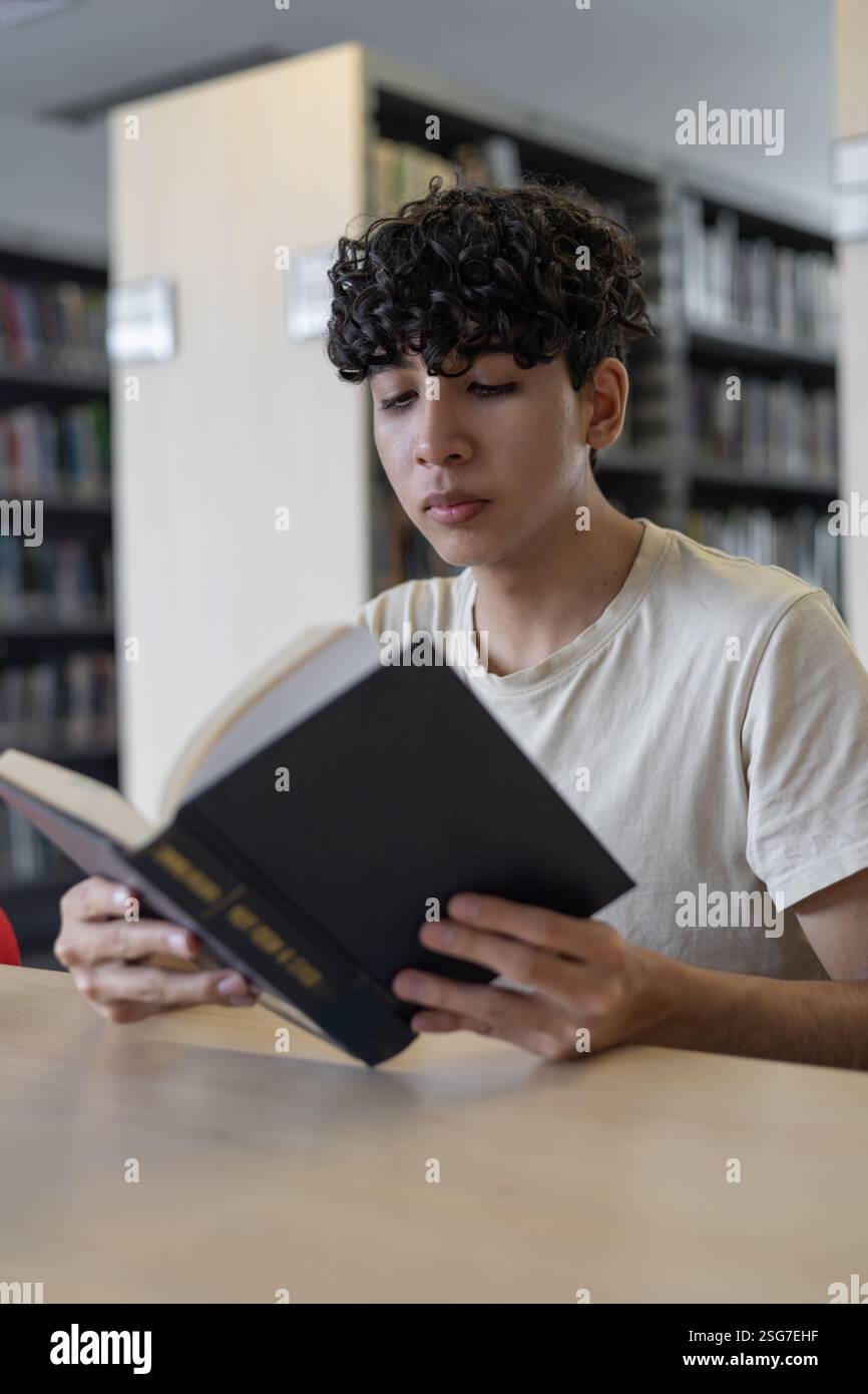 Un giovane concentrato che studia in una biblioteca tranquilla. Ideale per i temi dell'istruzione, della concentrazione, dell'apprendimento e della dedizione accademica. Foto Stock