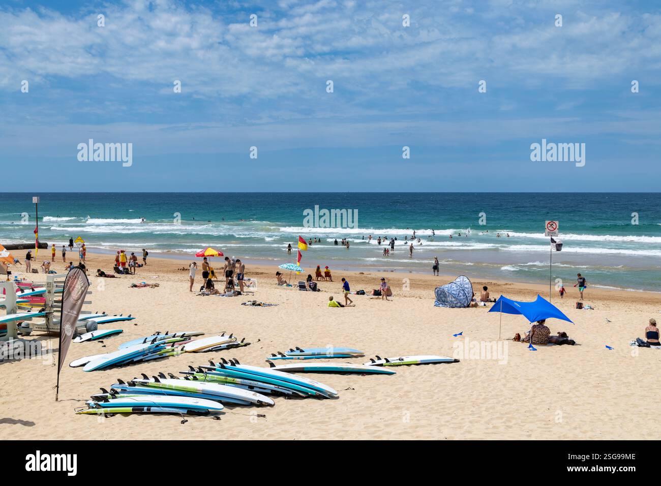 Manly Beach, Sydney, New South Wales, Australia. Le persone si rilassano sulla spiaggia accanto alle tavole da surf della scuola di surf, alle onde blu dell'oceano Foto Stock