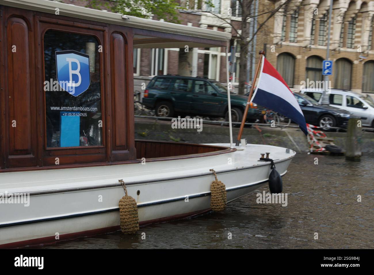 Amsterdam. La barca bianca naviga nelle acque calme, una bandiera rossa, bianca e blu che sventola orgogliosamente nel vento. Una scena di puro patriottismo sulla pittoresca ca Foto Stock