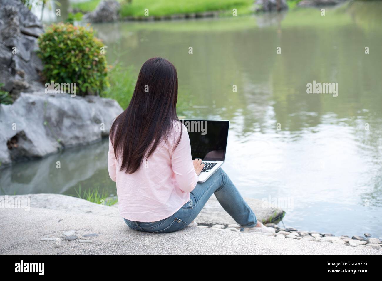 Donna asiatica seduta parco verde con computer portatile. Donna che lavora in un'azienda felice di un notebook che utilizza un notebook con le mani che digitano sulla tastiera Foto Stock