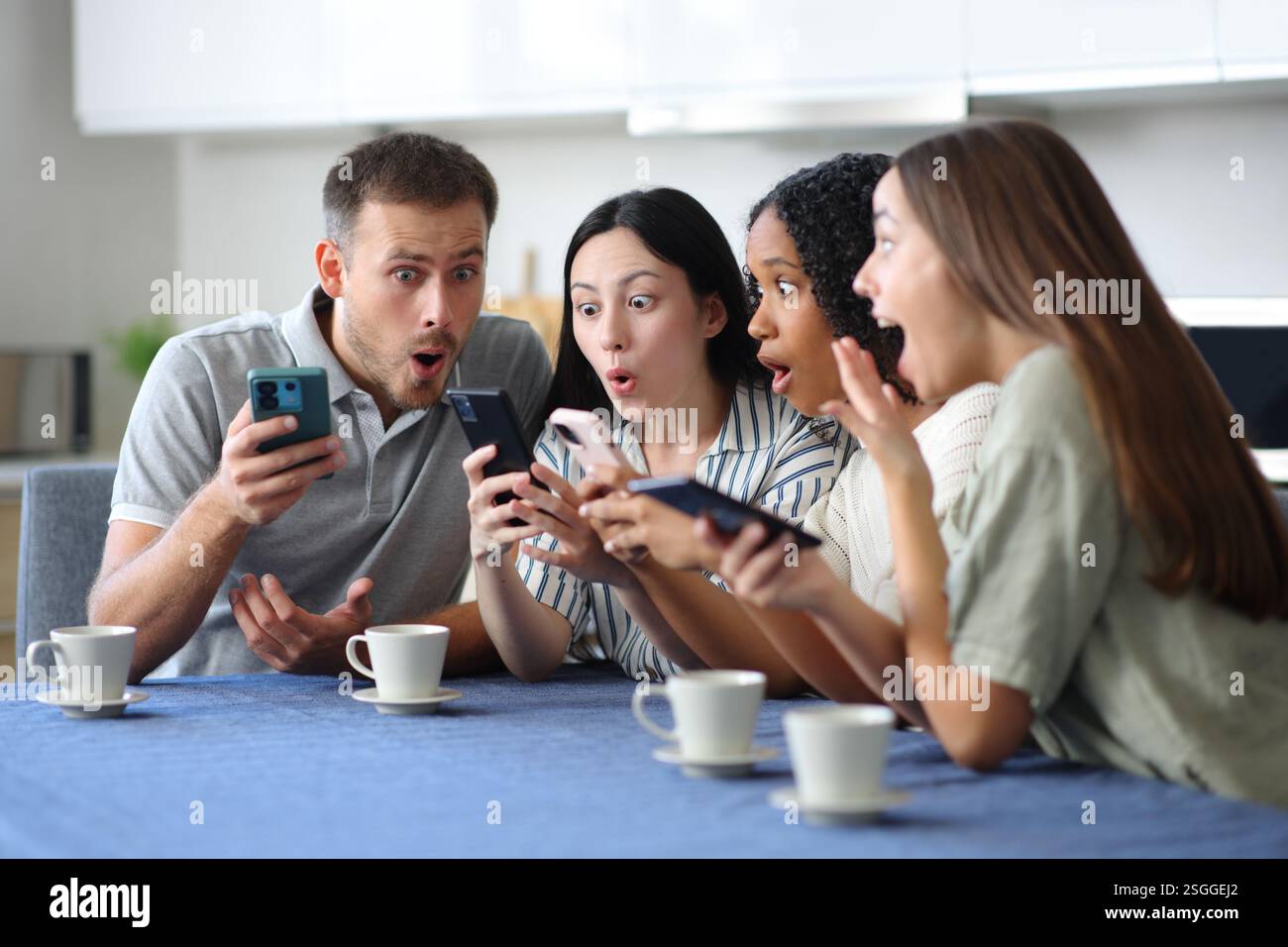 Un gruppo interrazziale di amici ha stupito mentre controllavano il telefono in cucina a casa Foto Stock