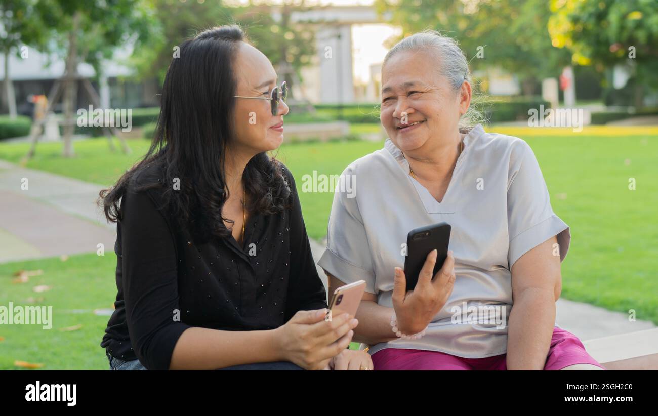 Ritratto di nonna felice e nonna si divertono a guardare le loro foto al telefono cellulare in un parco verde in una giornata di sole. Foto Stock