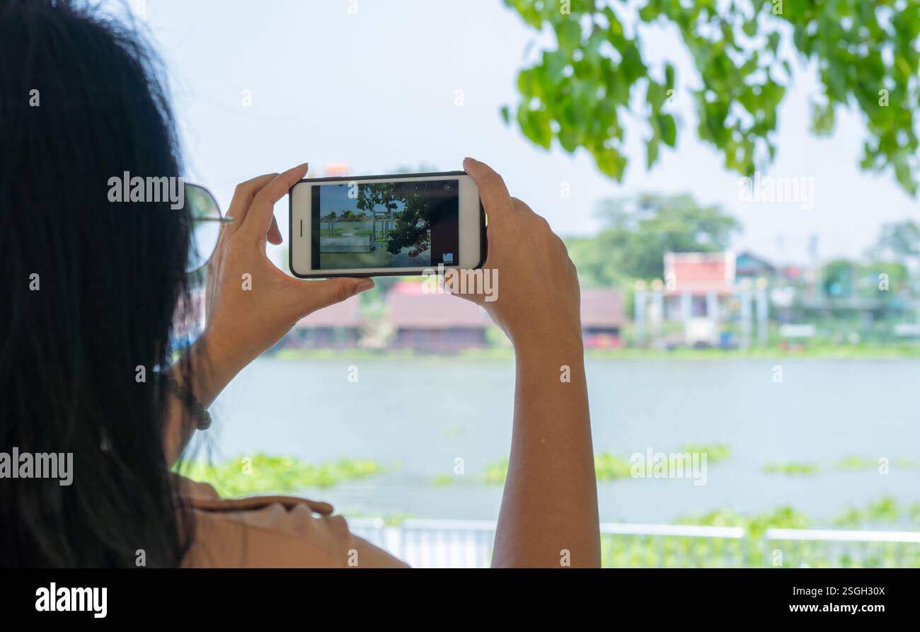 Donna asiatica scatta foto del fiume Chao Phraya, Thailandia, su uno smartphone, una vista dal retro. stile di vita attivo e impressioni Foto Stock