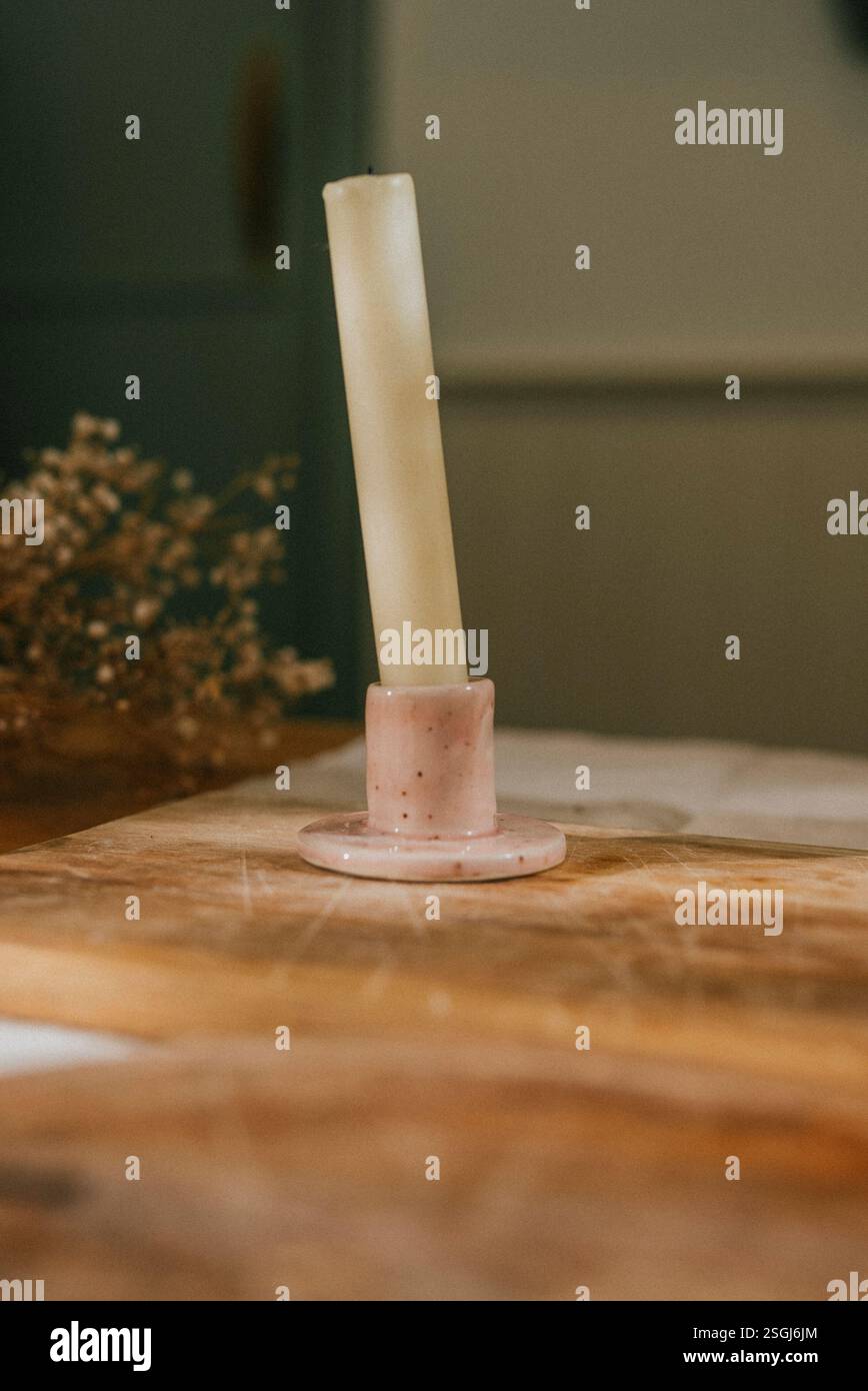 Una candela è posizionata su una base rosa su un tavolo di legno. La scena è semplice ed elegante, con la candela che fornisce un'atmosfera calda e invitante Foto Stock