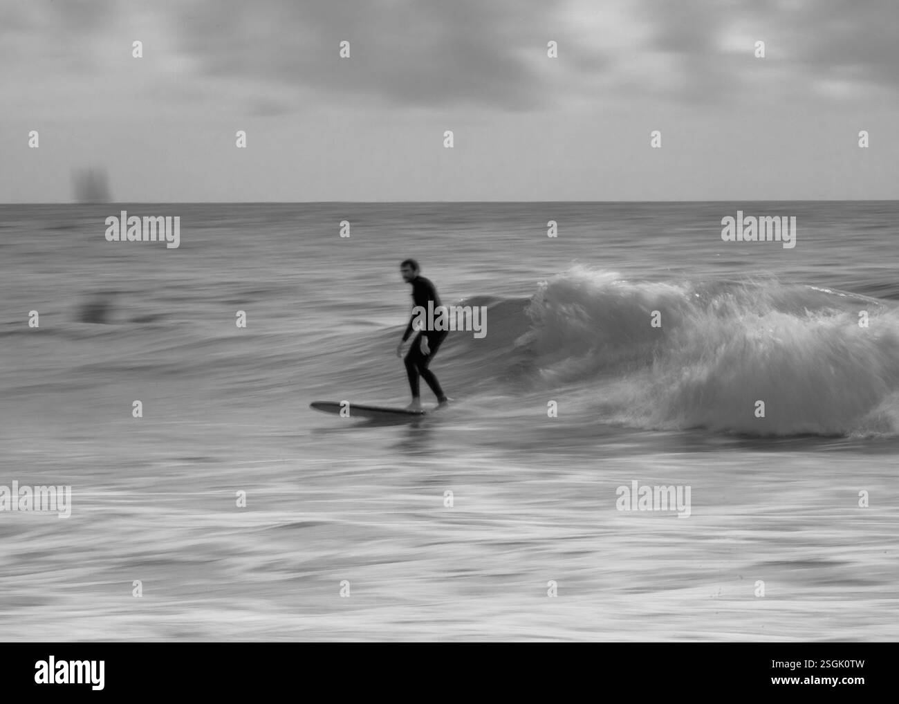 Immagine di un surfista nella sfocatura del movimento che cavalca un'onda in bianco e nero Foto Stock