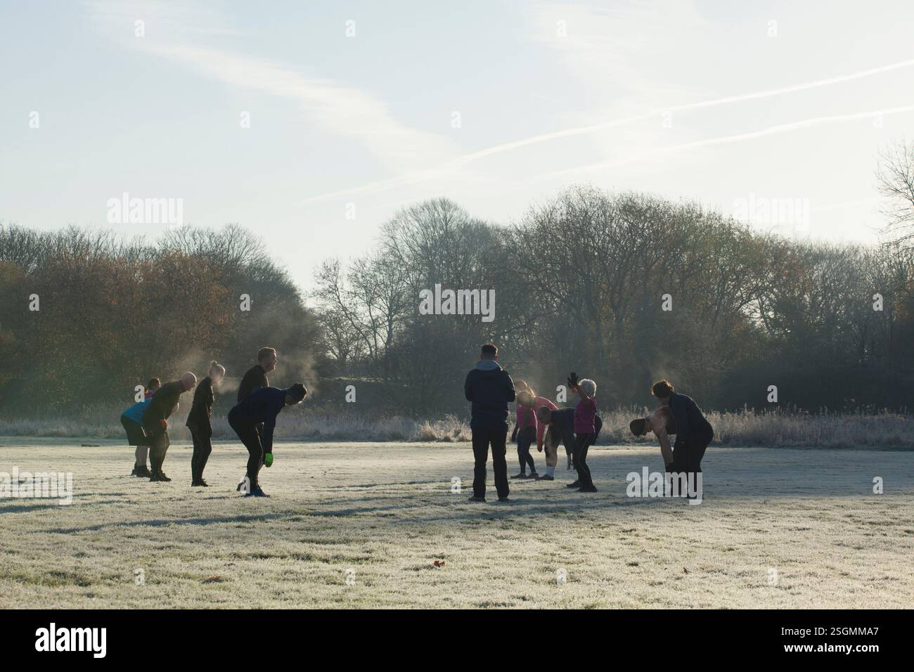 Un gruppo di persone si allenano all'aperto in un campo ghiacciato in una mattina fresca e soleggiata. Sale Water Park, Manchester, Regno Unito Foto Stock