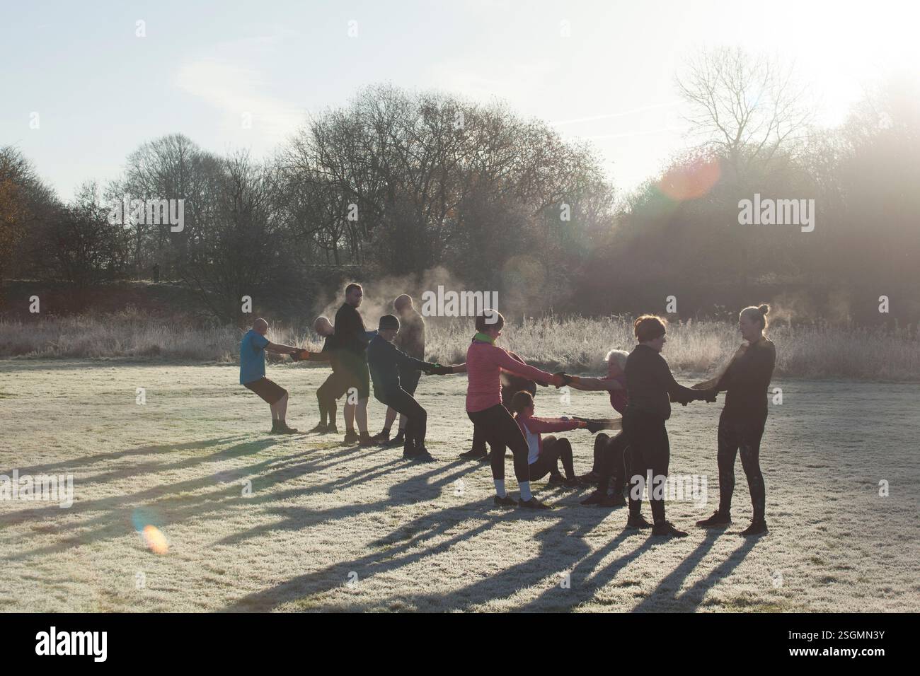 Un gruppo di persone che si allenano in un parco ghiacciato, tenendosi per mano in cerchio con il sole che sorge dietro di loro. Sale Water Park, Manchester, Regno Unito Foto Stock