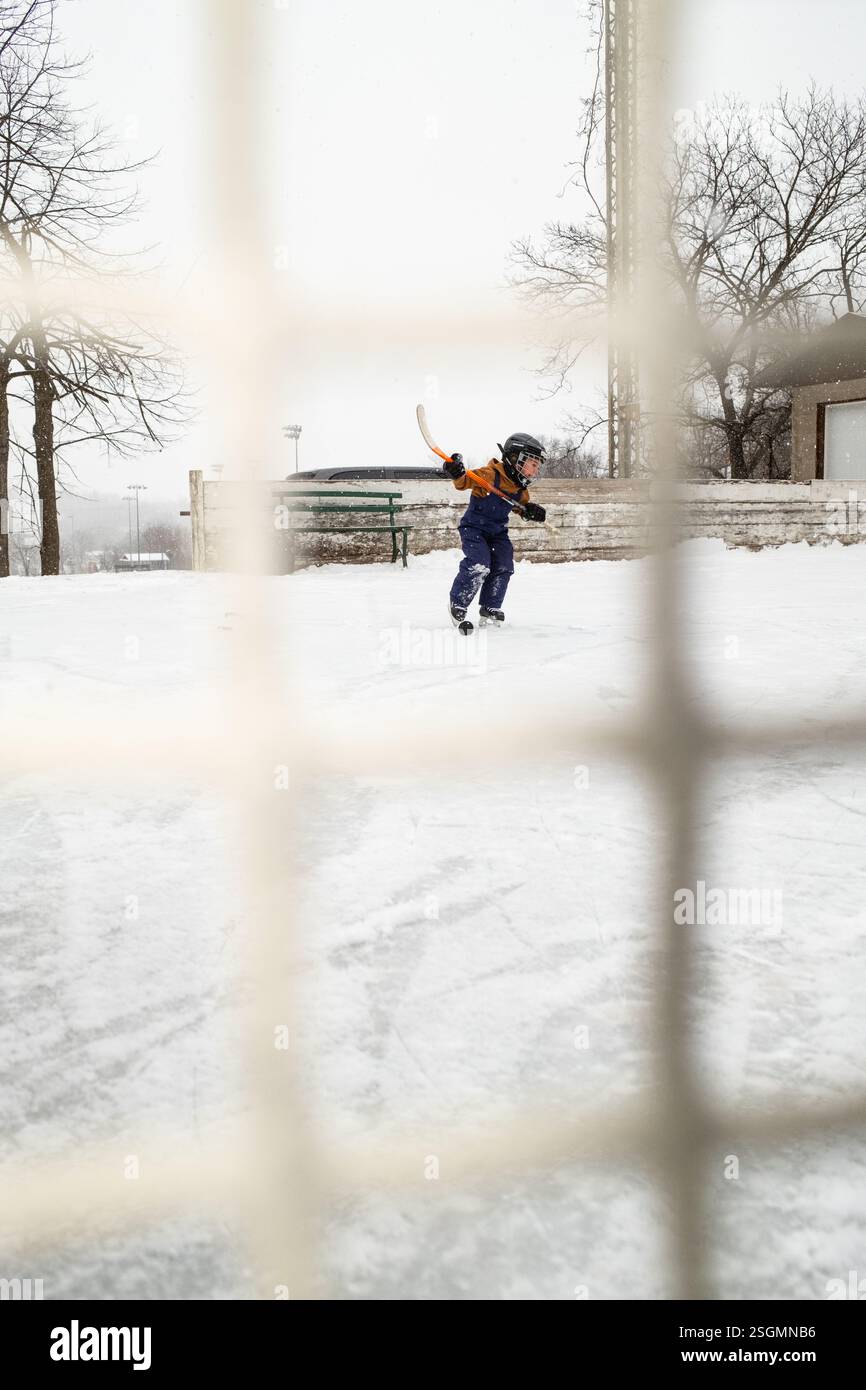 Bambini che giocano a hockey sulla pista di pattinaggio all'aperto in inverno Foto Stock