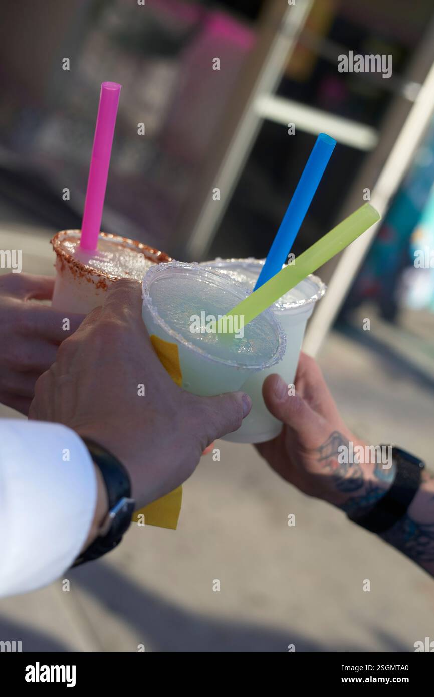 Tre mani che reggono colorate bibite di paglia in bicchieri di plastica all'aperto in una giornata di sole, Miami, Florida, Stati Uniti Foto Stock