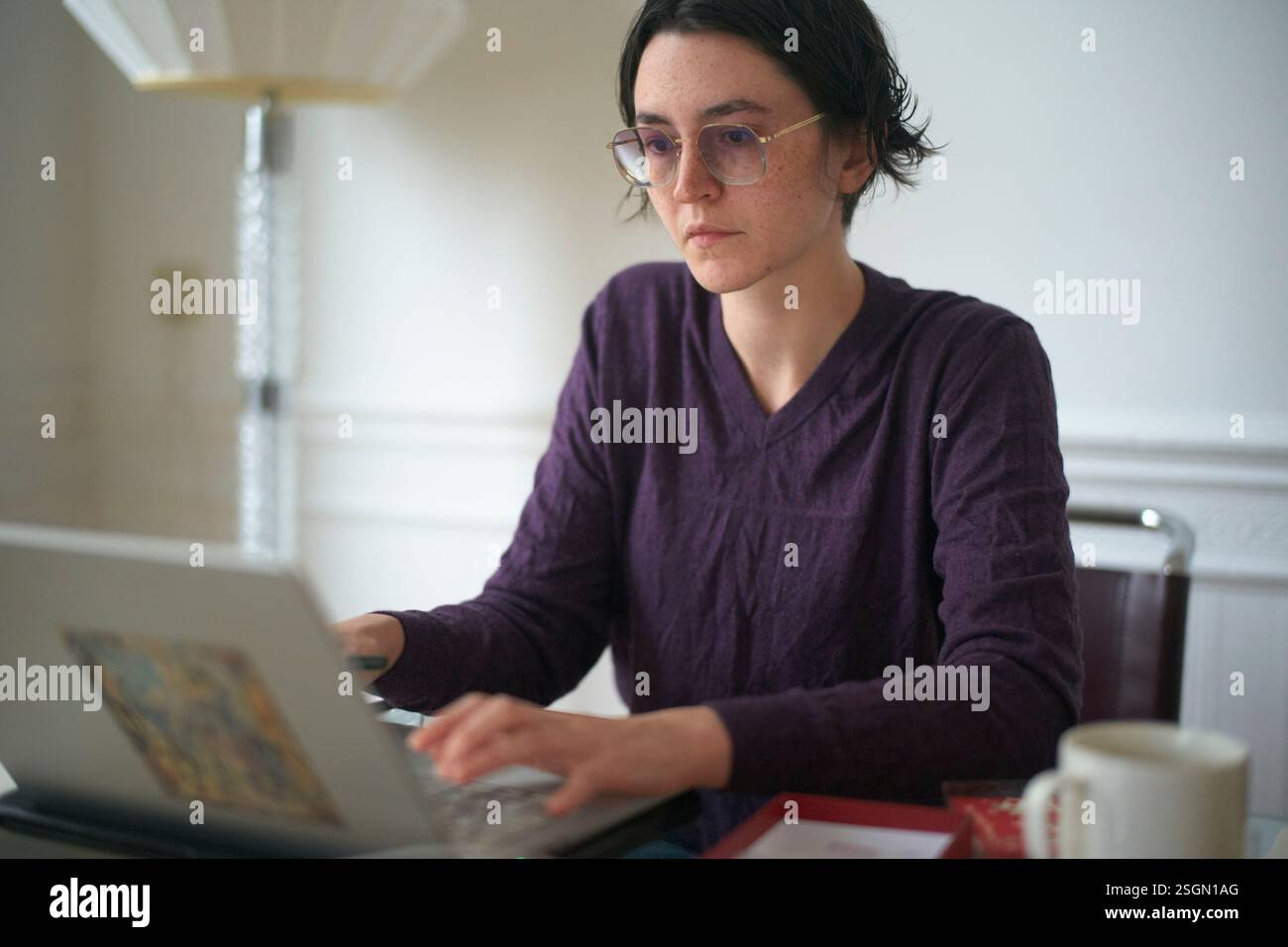 Donna molto concentrata che lavora su un notebook a un tavolo con una tazza e libri. Foto Stock