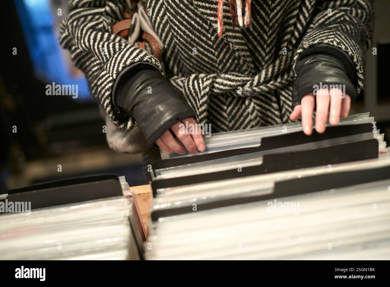 Donna che indossa un cappotto a spina di pesce che sfoglia dischi in vinile in un negozio. Foto Stock