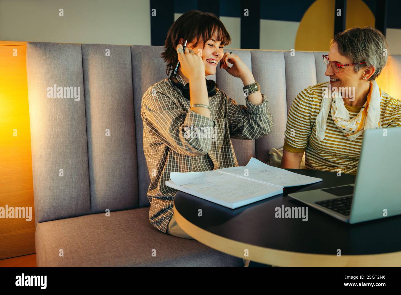 Un tutor e un allievo condividono un momento di gioia durante una sessione in classe extra, circondati da notebook e notebook, favorendo un ambiente di apprendimento positivo Foto Stock