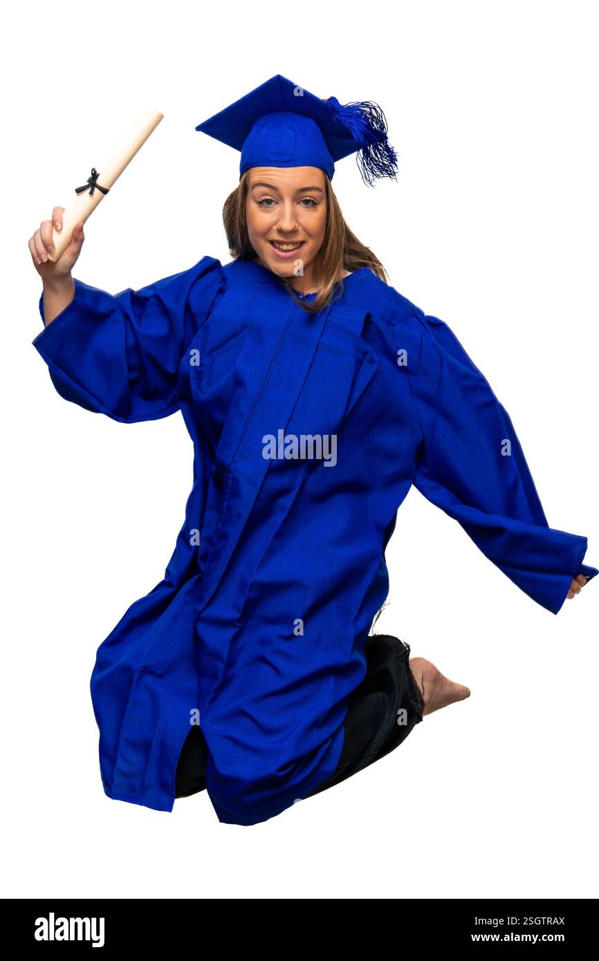 La giovane donna caucasica che indossa un abito blu si inginocchia e salta mentre tiene il diploma in festa, isolata su sfondo bianco Foto Stock