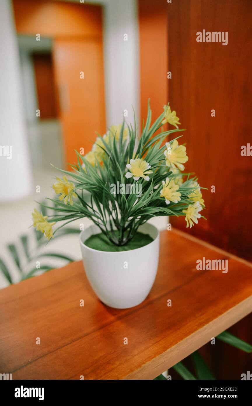 Fiori artificiali gialli in una pentola bianca su una mensola di legno. Foto Stock