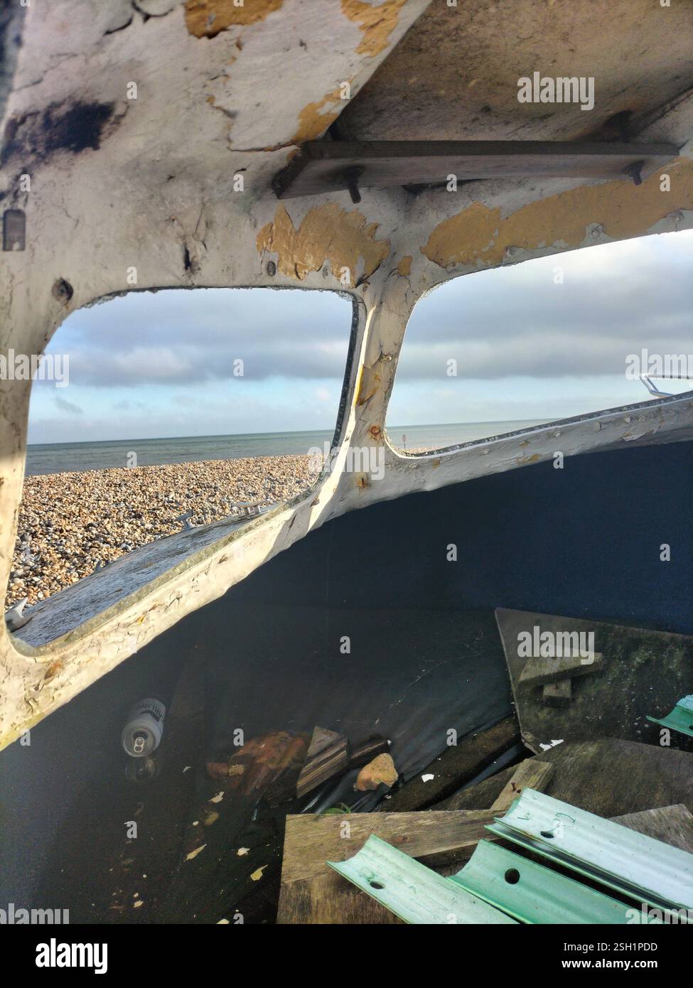 L'interno arrugginito della barca offre uno scorcio del mare in una giornata nuvolosa. All'interno di una vecchia barca, la vernice sbucciante rivela una vista della costa Foto Stock