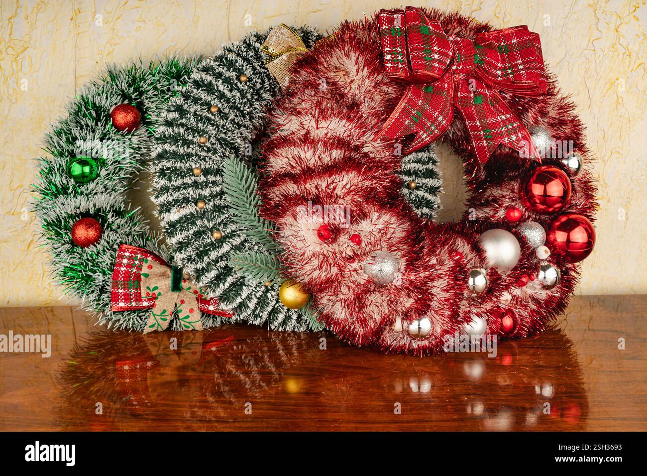 Lussureggiante corona di pino con frutti di bosco rossi contro il muro. Una splendida decorazione che simboleggia la gioia, il comfort e le tradizioni familiari. Foto Stock