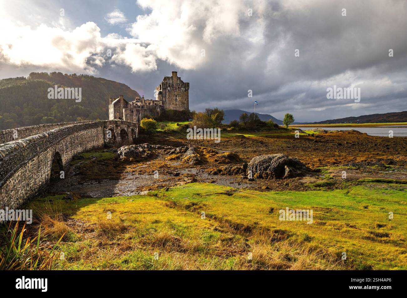 Castello di Eilean Donan e ponte di pietra sulla riva del loch sotto nuvole drammatiche nelle Highlands scozzesi Foto Stock