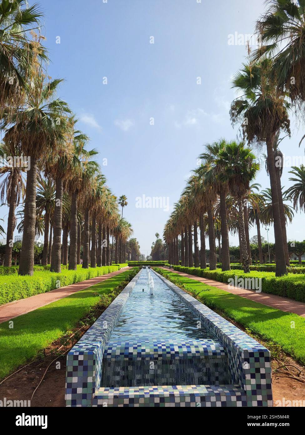 Vista panoramica del Parco della Lega Araba a Casablanca, Marocco, con fontana piastrellata e sentieri fiancheggiati da palme in un ambiente sereno. Foto Stock