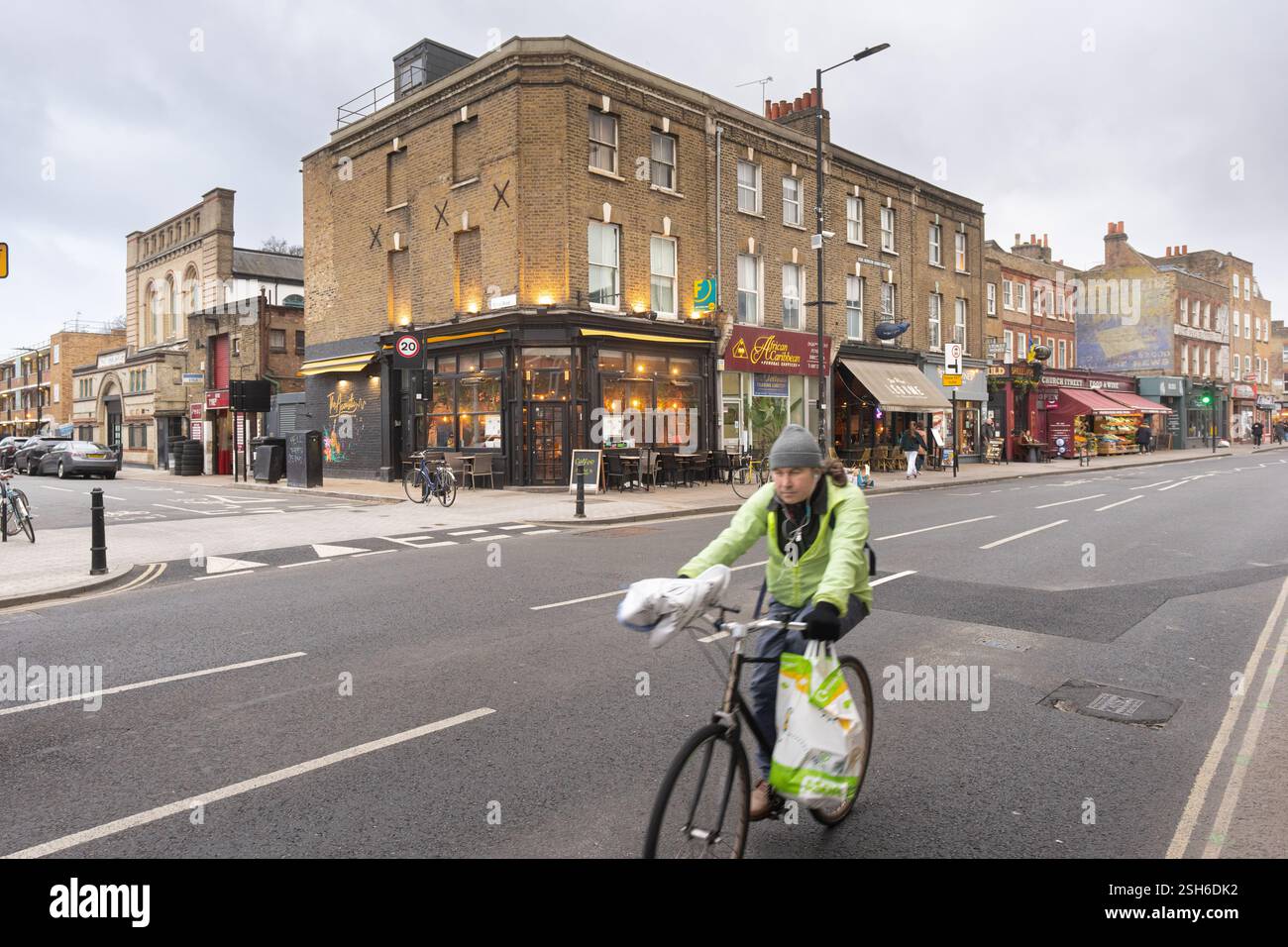 Ciclista su Stoke Newington Church Street, Londra, Regno Unito, vicino a un negozio all'angolo. Una persona guida una bicicletta carica di borse. Foto Stock
