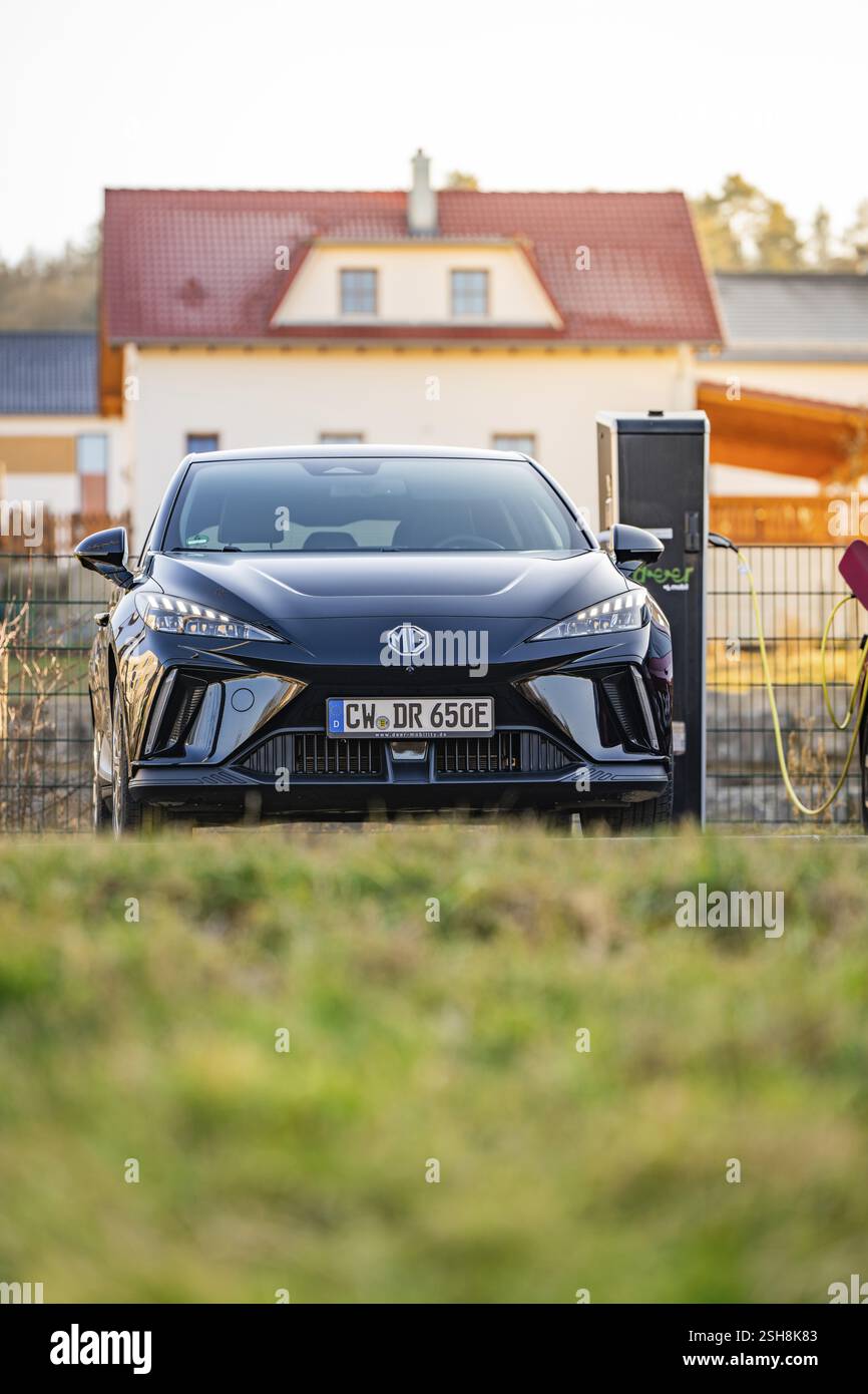 Un'auto elettrica nera è parcheggiata di fronte a una casa e viene caricata, Deer e- Carsharing Vehicle MG4, Calw District, Germania, Europa Foto Stock
