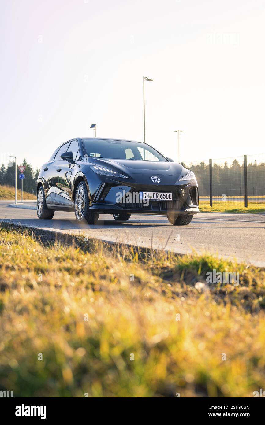 Auto nera che guida su una strada con prato, sole luminoso sullo sfondo, veicolo condiviso con Deer Mobility, Gechingen, Foresta Nera, Germania, Europ Foto Stock