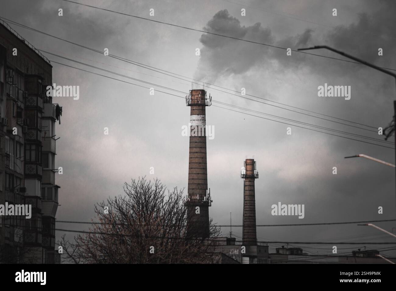 Un paesaggio urbano con camini industriali che eruttano fumo contro un cielo grigio e coperto. I cavi elettrici creano un contrasto urbano. Foto Stock