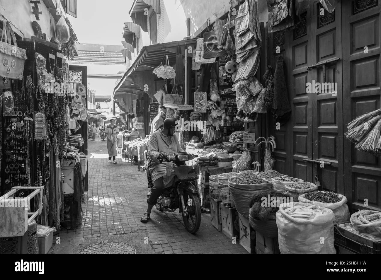 Uomo in abiti tradizionali con cappuccio, chilava, in sella a una motocicletta in un mercato marocchino di souk nella medina, vita di strada. Foto Stock