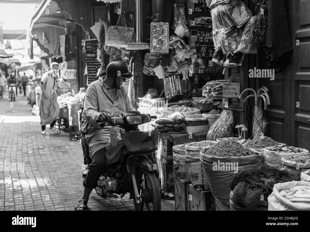 Uomo in abiti tradizionali con cappuccio, chilava, in sella a una motocicletta in un mercato marocchino di souk nella medina, vita di strada. Foto Stock