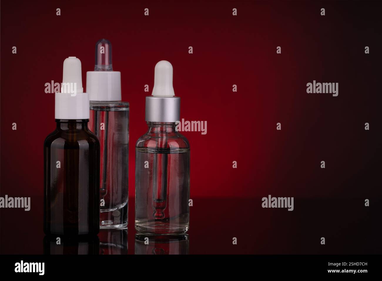 Tre flaconi contagocce in vetro con design diversi su sfondo rosso Foto Stock