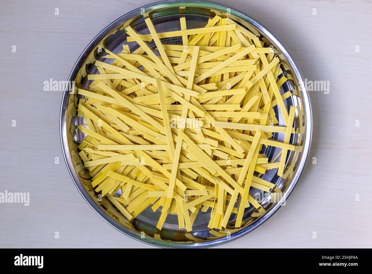Spaghetti piatti crudi su una piastra di acciaio, sparati dall'alto. Sfondo in legno chiaro. Foto Stock