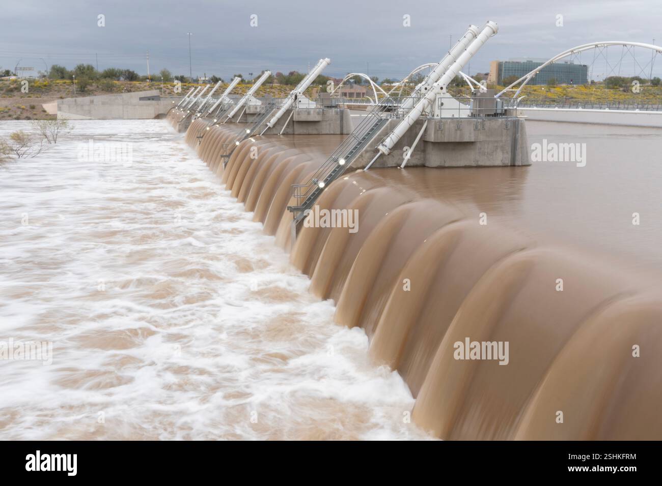 Una potente corsa d'acqua scorre attraverso la struttura in cemento di una diga, mostrando sia la forza naturale del fiume che la forza industriale di Foto Stock